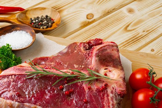 Raw t-bone meat with fresh vegetables and rosemary on the table, close up.