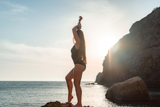 Young woman in swimsuit with long hair practicing stretching outdoors on yoga mat by the sea on a sunny day. Women's yoga fitness pilates routine. Healthy lifestyle, harmony and meditation concept.