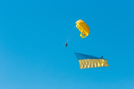 Parashutist in the blue clear sky flies with the Ukrainian national symbol flag background.