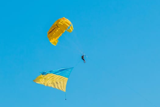Parashutist in the blue clear sky flies with the Ukrainian national symbol flag background.