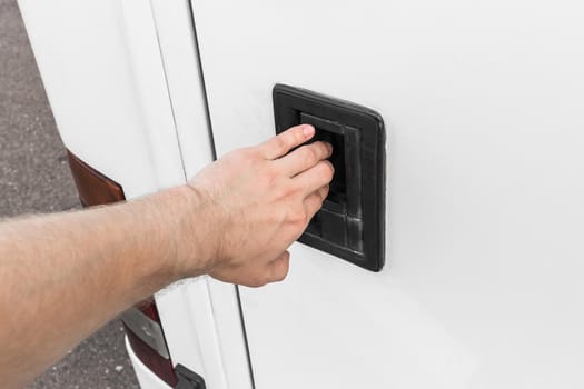 A man's hand opens or closes the luggage compartment of a vehicle, car or bus by the door handle.