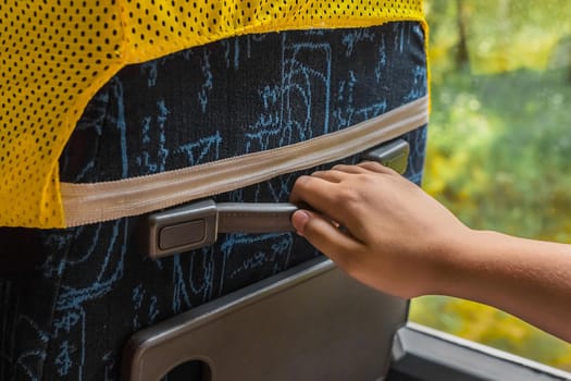 The girl's hand is holding on to the rubber handle of the seat on the bus, close-up.