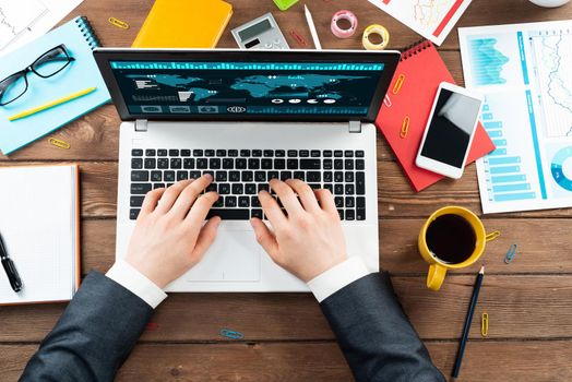 Close up businessman hands working at laptop. Top view office workplace with computer and financial documents on wooden table. Business occupation design with man in business suit sitting at desk