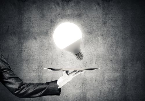 Cropped image of waitress's hand in white glove presenting glowing lightbulb on metal tray
