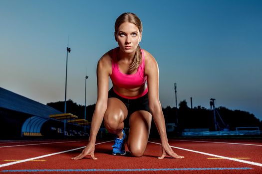 Portrait of beautiful woman ready to start running. Female athlete sprinter doing a fast sprint for competition on red lane at an outdoor field stadium.