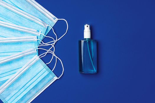 Pile of medical face masks with hand sanitizer on blue background close up
