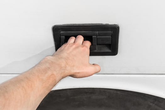 A man's hand opens or closes the luggage compartment of a vehicle, car or bus by the door handle.