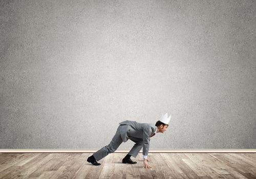 Young handsome businessman wearing white paper crown running in a hurry
