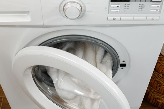 Washing machine with laundry on blue wall background, close up.