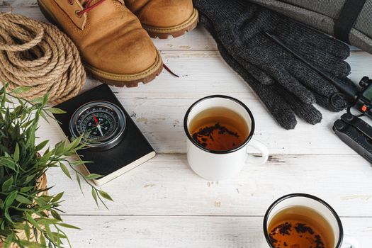 Hiking boots with equipment for hiking, cup of tea on wooden board close up