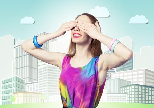 Redhead beautiful girl closing her eyes with hands. Charming lady wears bright dress and bracelets standing on background cartoon cityscape. Portrait of happy young woman waiting for pleasant surprise