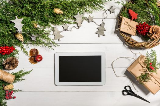 Juniper branches with a Christmas decor. Christmas, New Year background. Coniferous branches of juniper and white tablet with black screen. Top view, flat design. Christmas tree on white wooden background.