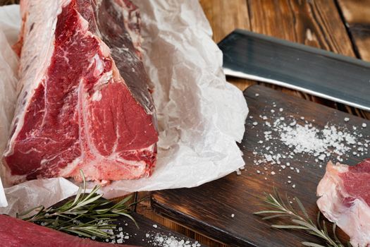 Raw T-bone steak with herbs on wooden board, close up