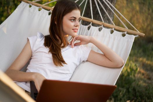 cheerful woman lies in a hammock with a laptop freelance nature. High quality photo
