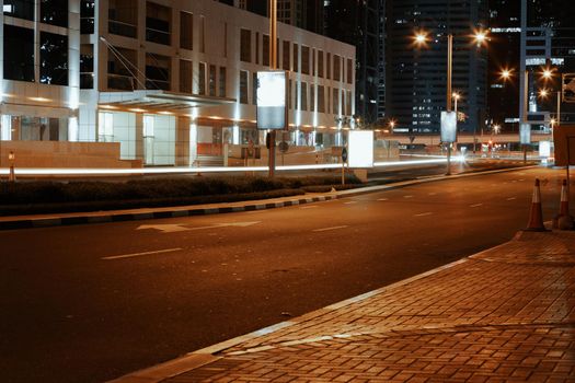 Empty asphalt road with modern buildings at night in Dubai, UAE