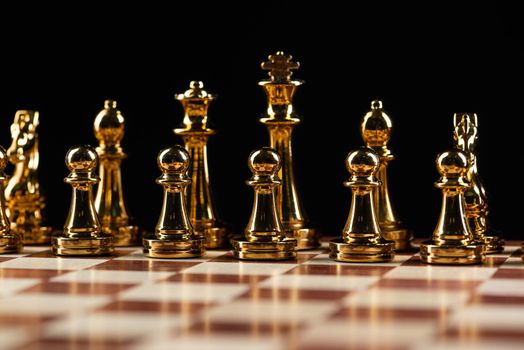 Golden chess figures standing on chessboard. Intellectual and tactic game. Strategy planning, leadership and teamwork business concept. Close-up gold chess pieces in row on black background.