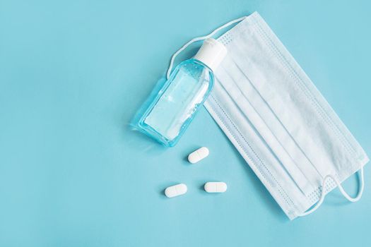 Respiratory mask, atibacterial hand treatment and medicine in capsules on blue background.Virus prevention and treatment.