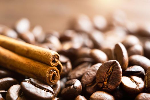 A stick of cinnamon lies on the roasted coffee beans close-up - fragrant macro backgrounds. Brown arabica coffee beans are scattered on the wooden table. Copy space