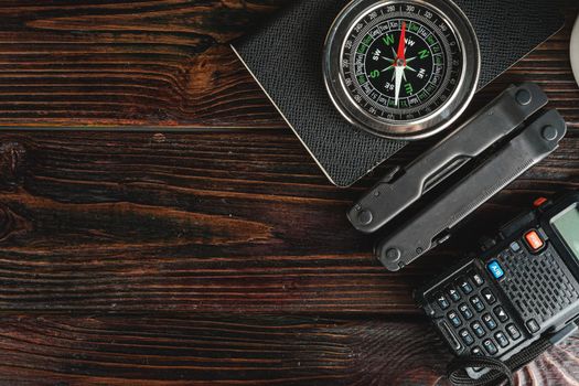 Compass surrounded by mountain gear tools on wooden background, closeup