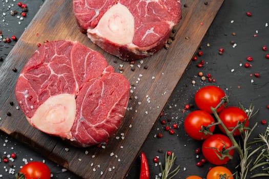 Two raw fresh marbled meat steak on dark background, cherry tomatoes and spices. Close up.