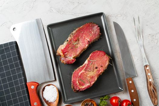 Marinated raw steaks on stone table with spices close up