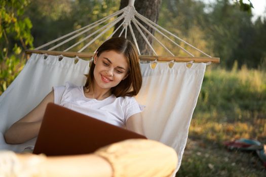 cheerful woman lies in a hammock with a laptop vacation internet travel. High quality photo