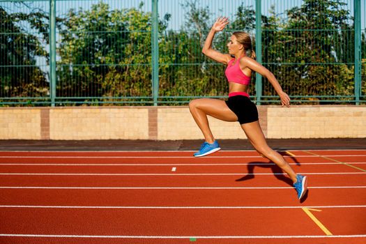 Side view beautiful young woman exercise jogging and running on athletic track on stadium. Sport, healthy lifestyle concept.