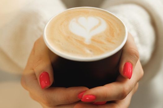 Female hands in sweater holding a cup of latte coffee close up