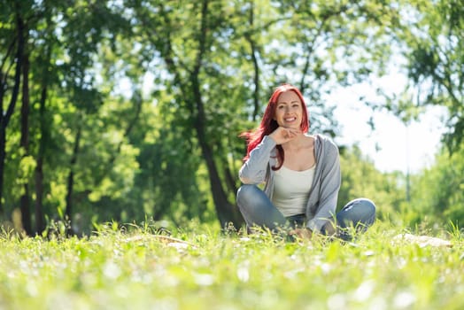 Portrait of a young attractive woman. Sitting in the park on the grass cross-legged