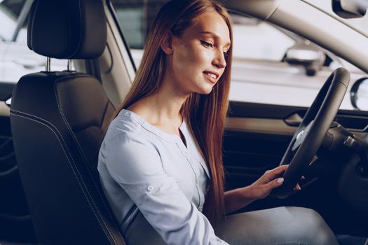 Attractive young woman sitting in new car in showroom close up