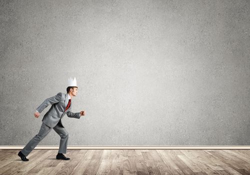 Young handsome businessman wearing white paper crown running in a hurry