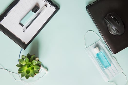 Top view of a desktop with notebooks, pens, and a laptop. Work from home using an online device, protection from coronavirus during the quarantine period. Protective masks and antiseptic on a mint background.