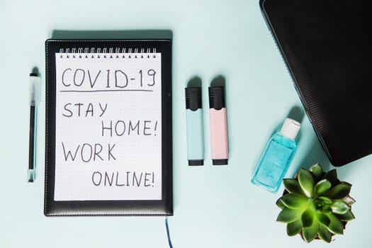 Top view of a desktop with notebooks, a markers, and a laptop. Text Covid-19, stay at home, WORK ONLINE. Work from home, protection from coronavirus during the quarantine period. Mint background.