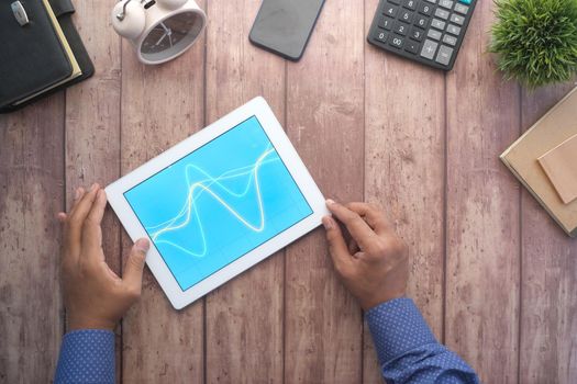 man's hand working on digital tablet at office desk, using self created chart.