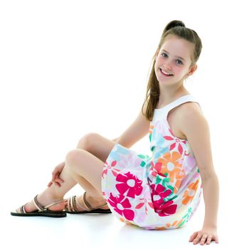 A teenage girl in a short dress sits on the floor and holds her knees with her hands. The concept of beauty, people, fashion. Isolated on white background.