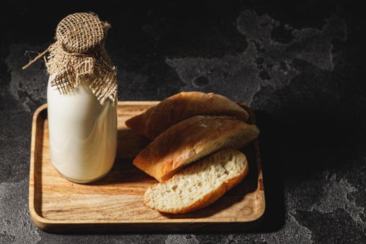 Glass bottle of milk with sliced baguette bread on dark background