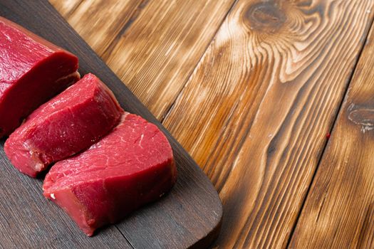 Slices raw meat fillet on wooden board, close up