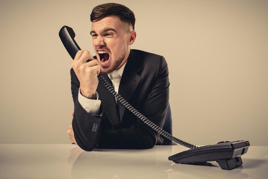 A young man in a black suit dials the phone number while sitting in the office. Manager talking on the phone. Man emotionally shouts