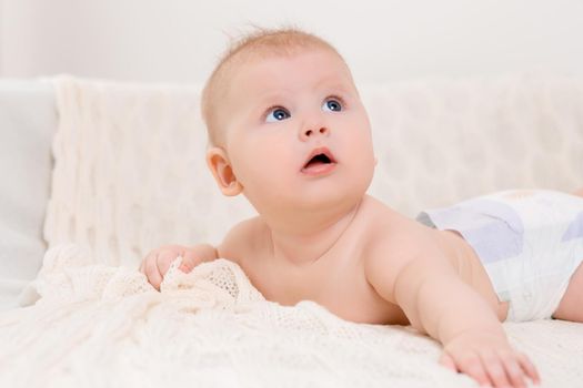 Happy baby lying on a white plaid in the bedroom. Sweet baby in a diaper