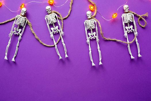 Halloween layout of garland of skeletons on a rope, glowing Jack o Lantern, pumpkins on a purple background. Flat lay horror and a terrible holiday 