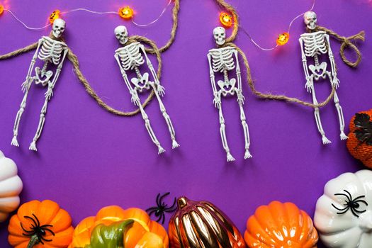 Halloween layout of garland of skeletons on a rope, glowing Jack o Latern, pumpkins, spiders on a purple background. Flat lay horror and a terrible holiday 
