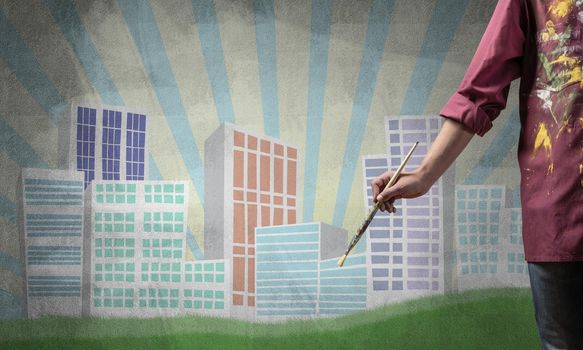 Close up artist hand holding paintbrush. Painter in shirt standing on background colorful picture of city. Modern downtown with high office buildings artwork. Creative hobby and artistic occupation.