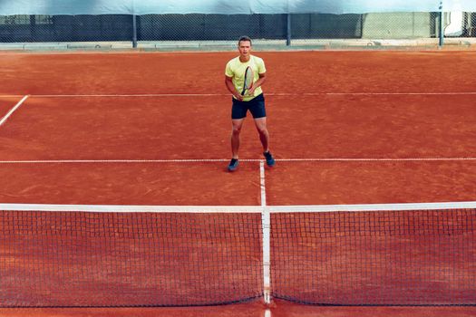Young handsome man playing tennis on the clay tennis court
