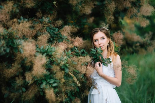 Happy girl in a turquoise long dress in a green park on a background of herbs, trees and rose bushes