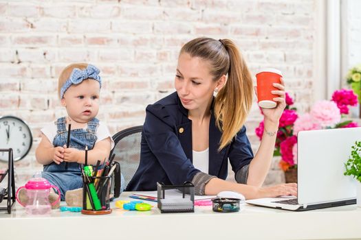 Businesswoman mother woman with a daughter working at the laptop. At the workplace, together with a small child