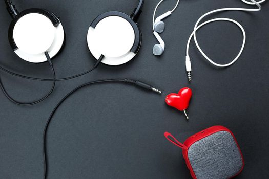 A heart-shaped headphone splitter for a couple in love. Connected to red portable speaker and two pairs of headphones - flat lay. Valentine's day, love, modern technology, copy space, black background