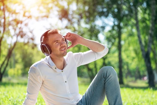 Young man in the park listens to music. He sits on the grass and enjoys music.
