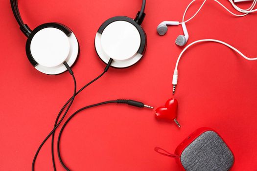 A heart-shaped headphone splitter for a couple in love. Connected to a red portable speaker and two pairs of headphones - flat lay. Valentine's day, love, modern technology, copy space