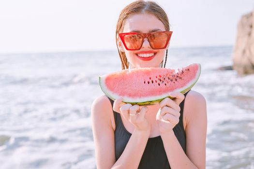 cheerful woman in sunglasses eating watermelon by the ocean. High quality photo