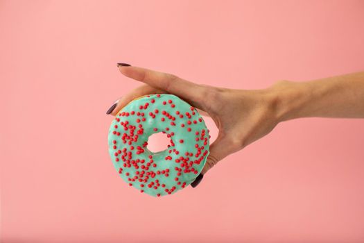 Crop female hand holding sweet blue donut isolated on pink background